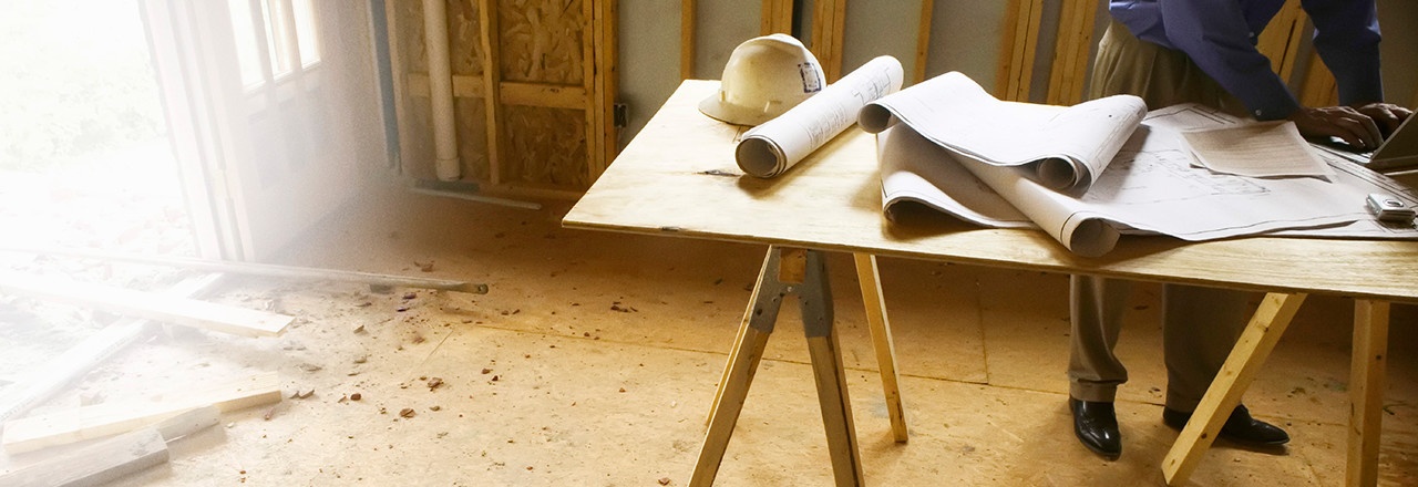 Home Builder Working on laptop with blueprints on a table