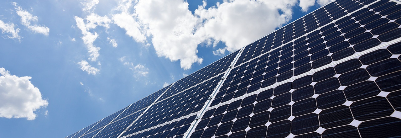 Black solar panels set against a blue, partly cloudy sky