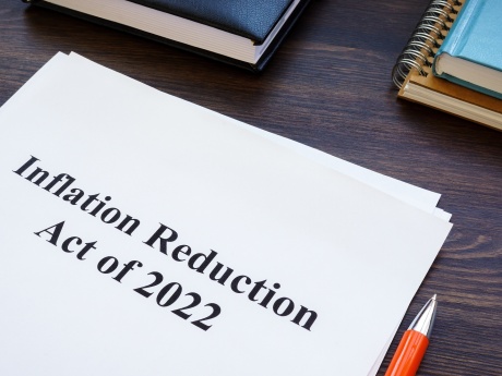 Sheet of paper reading "Inflation Reduction Act" on desk with books, pen and notebook