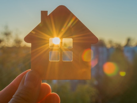 Someone holding a small house cutout with the setting sign shining through it